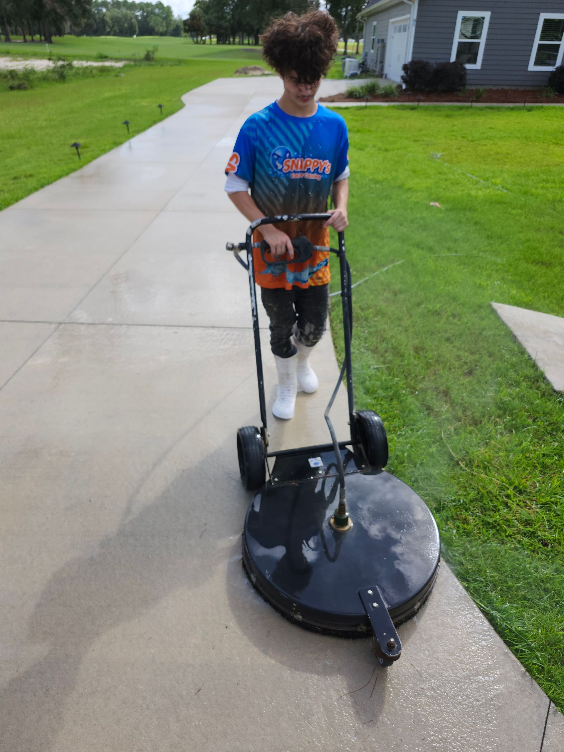 Teenager power washing a concrete driveway on a sunny day.
