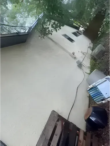 Tan building exterior with white trim; items on ground; trees overhead.