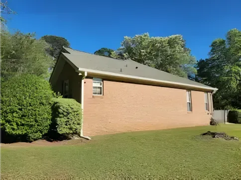 Brick house with a green roof and lawn, under a clear blue sky.