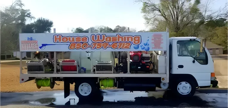 House washing truck parked on a wet surface. White cab, orange and blue logo.