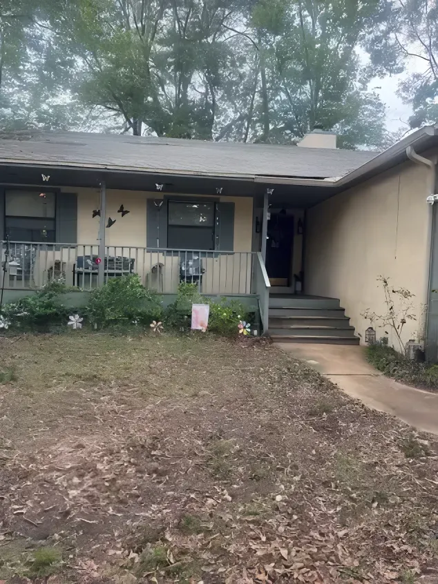 A one-story house with a covered porch, steps leading to the door, and a yard with dry leaves.