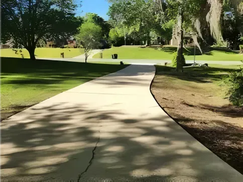 Cement pathway winding through a park with trees and green grass under a bright sunny sky.