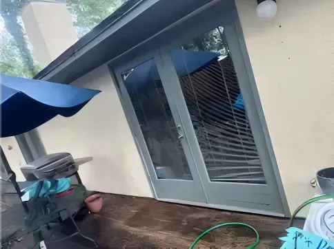 Exterior of a house with gray french doors, patio, a blue umbrella, and a hose.