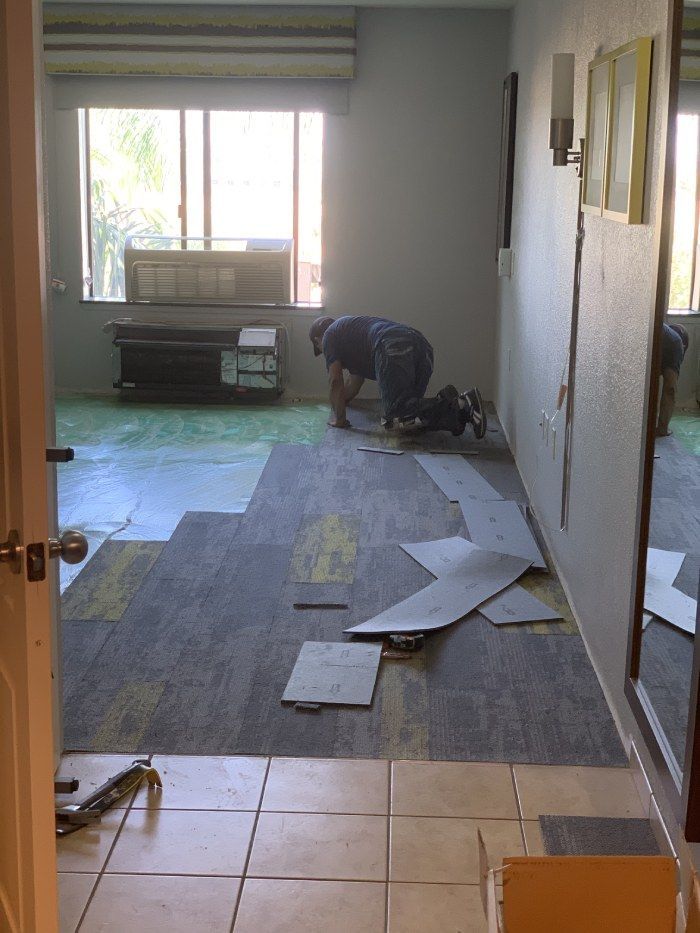 A man is installing a carpet in a living room.
