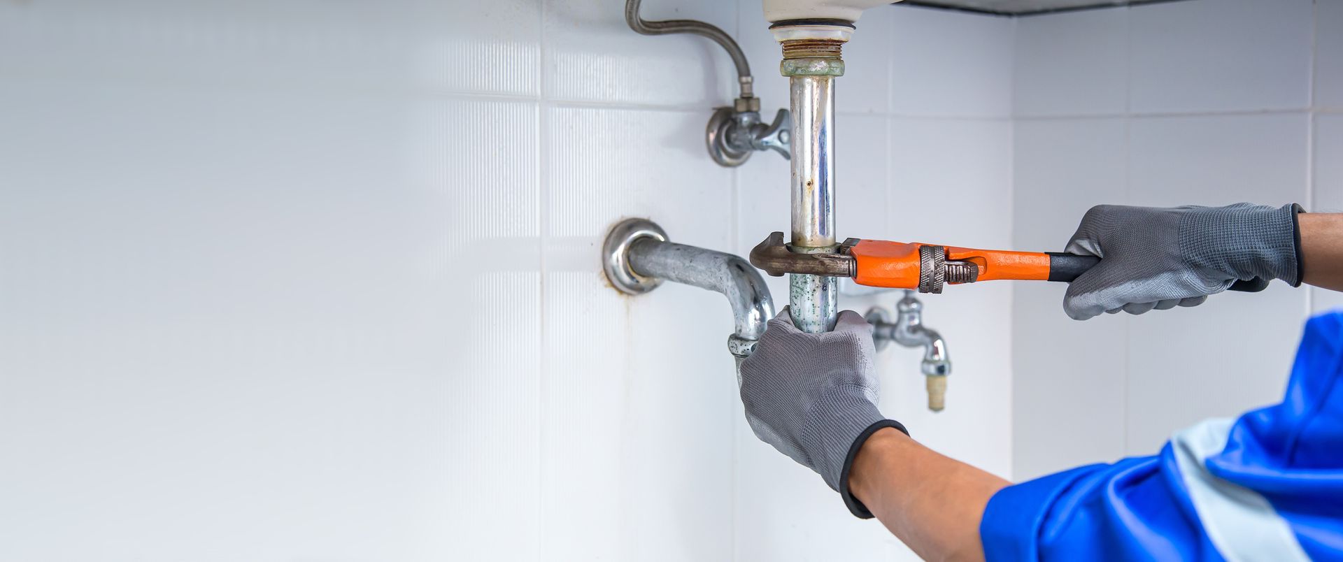 A plumber is fixing a sink with a wrench.