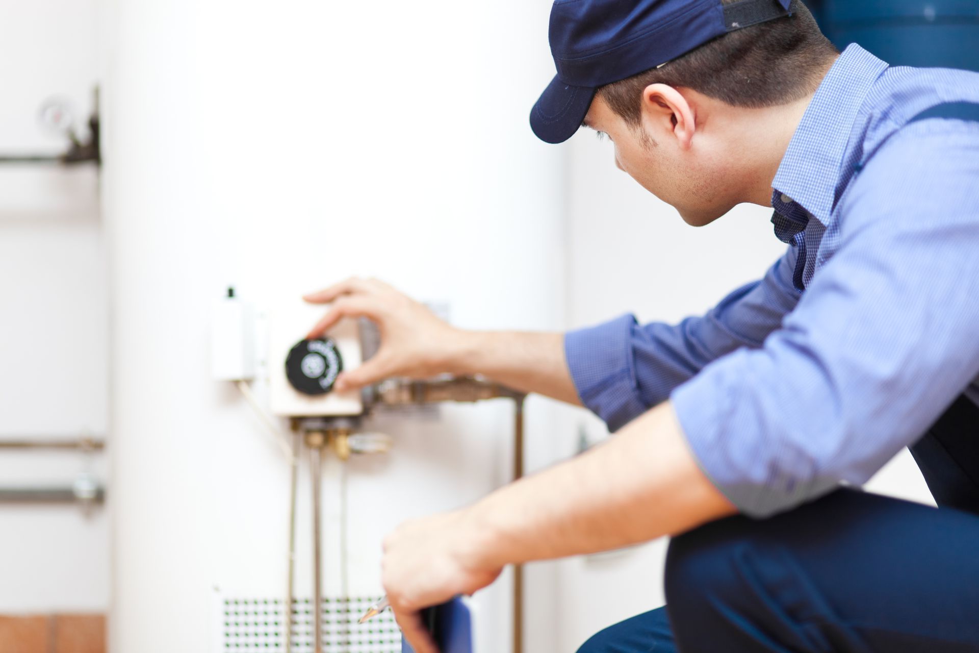 A man is kneeling down fixing a water heater.