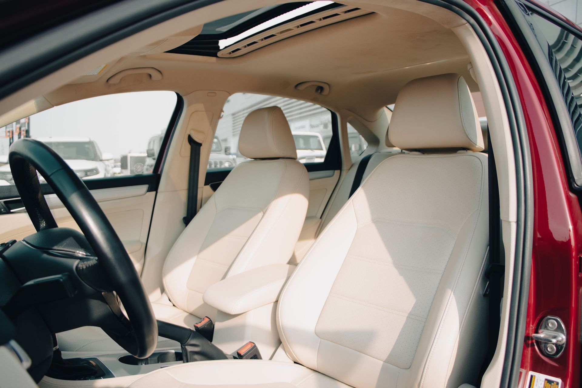Car interior with beige seats and steering wheel, viewed through an open red door