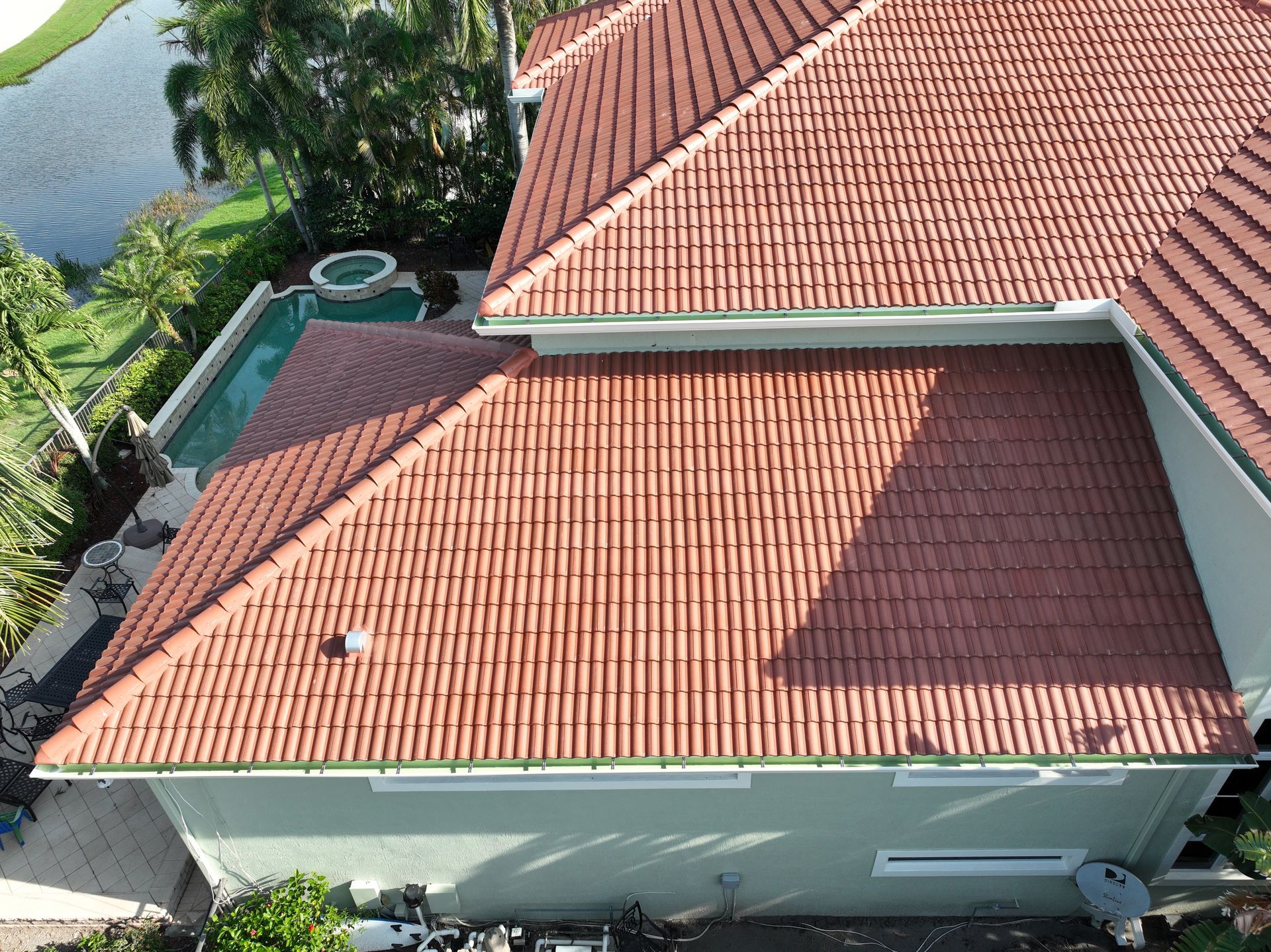 Red tiled roof on a green house next to a body of water.