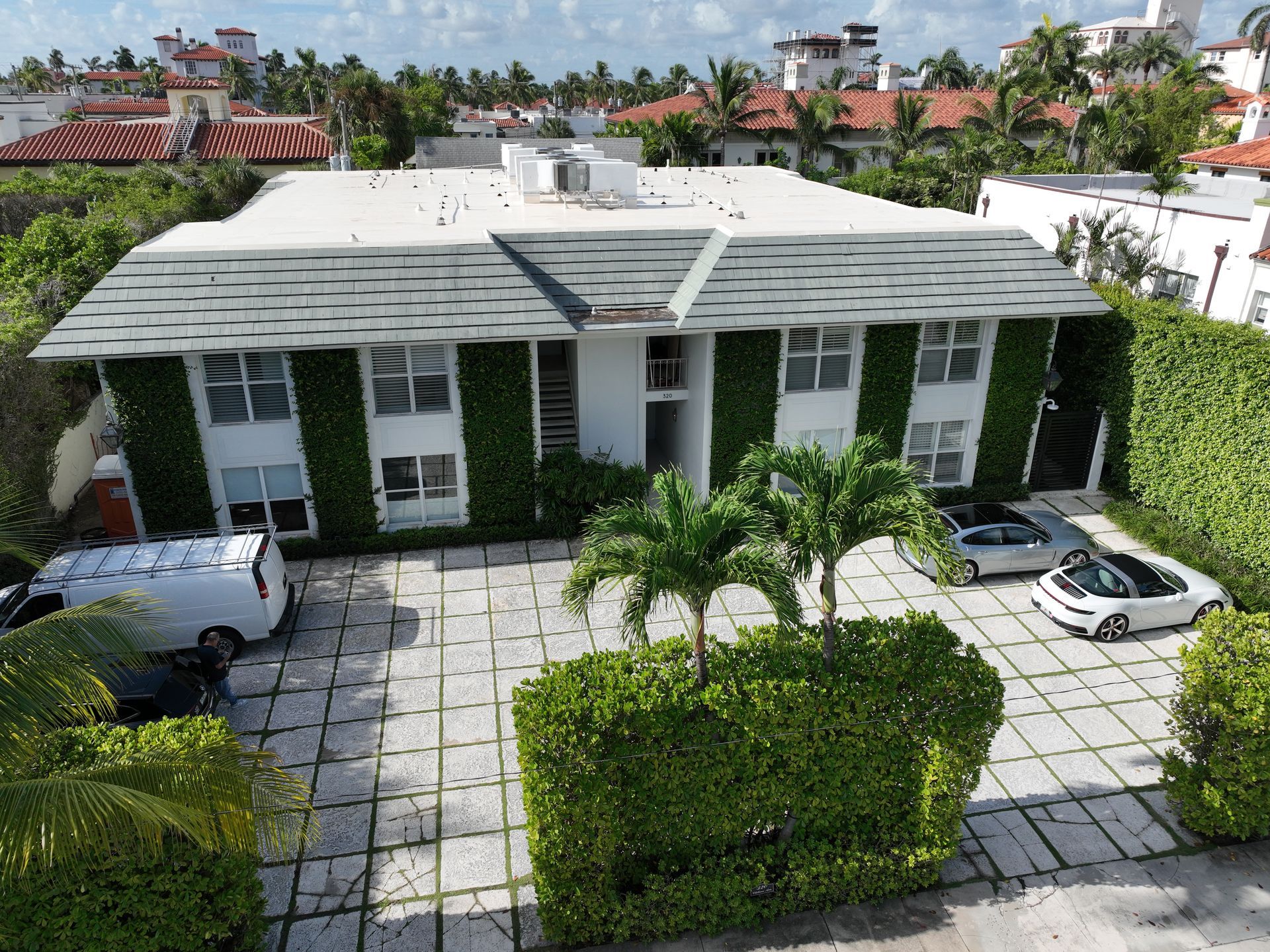 Two-story white building with ivy, palm trees, and cars parked in front.
