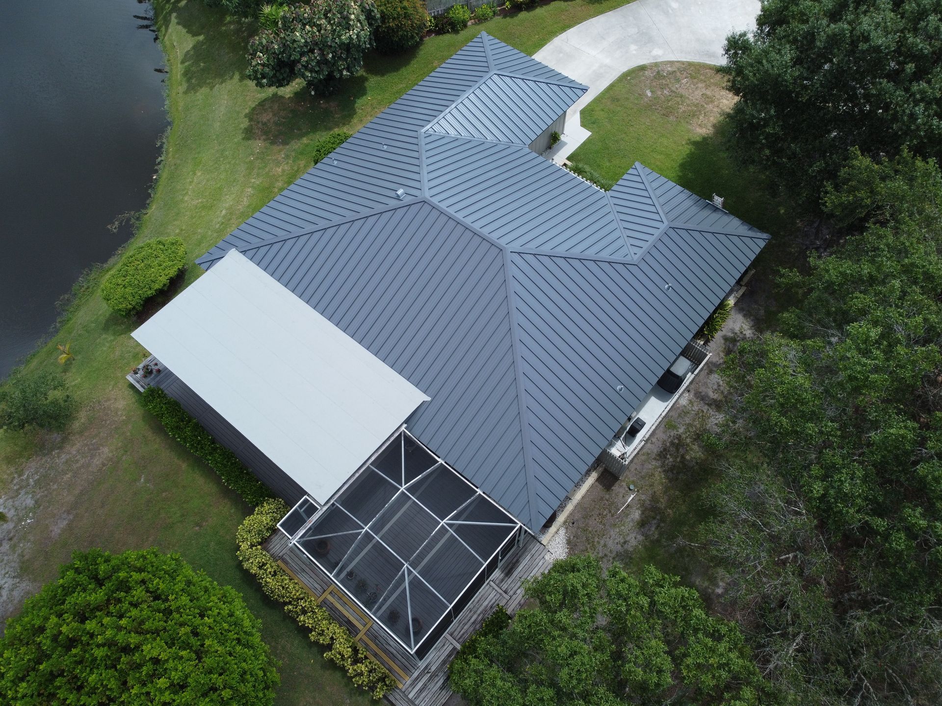 Aerial view of a house with a gray metal roof, a white patio cover, and a pool enclosure.