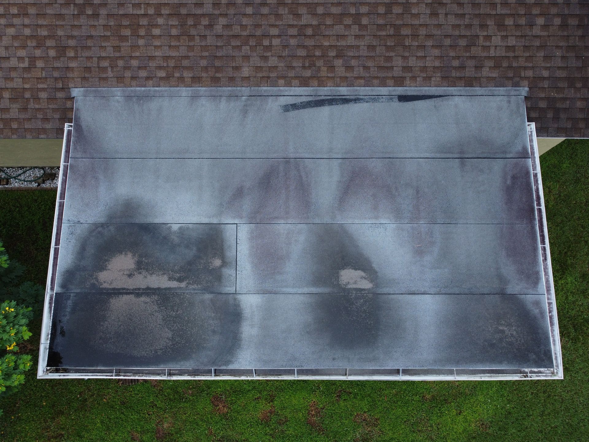 Overhead view of a flat roof with dark discoloration and a lighter area on green grass.