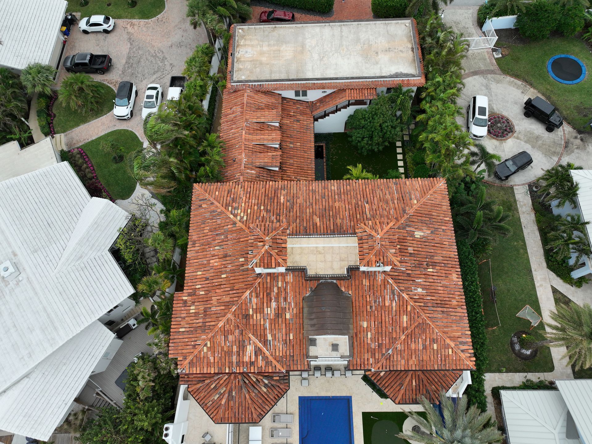 Aerial view of a house with a terracotta tile roof, pool, and parked cars.