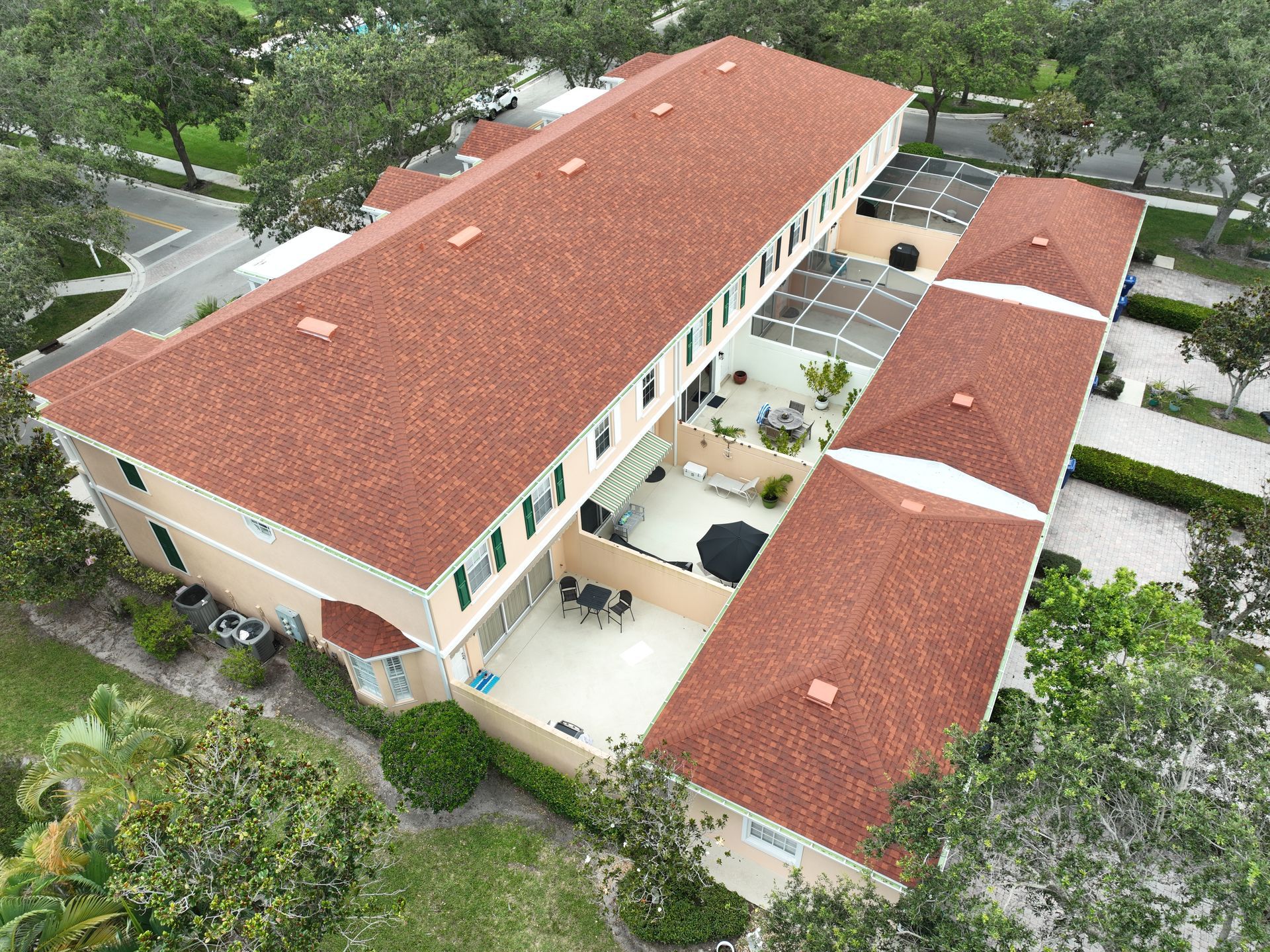 Aerial view of a multi-unit building with terracotta roofs and patios, surrounded by greenery.