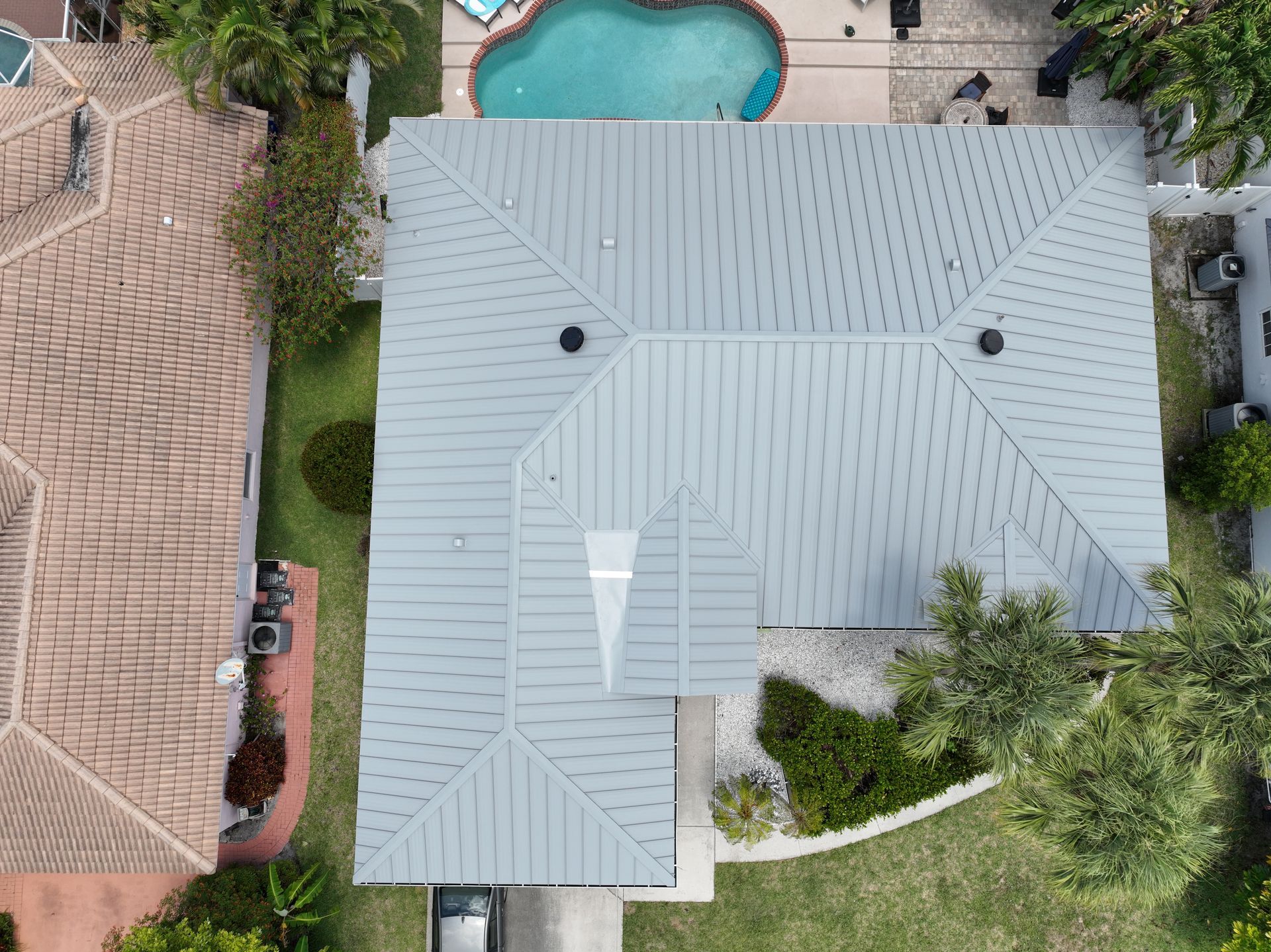Aerial view of a house with a gray roof, pool, and surrounding landscaping.