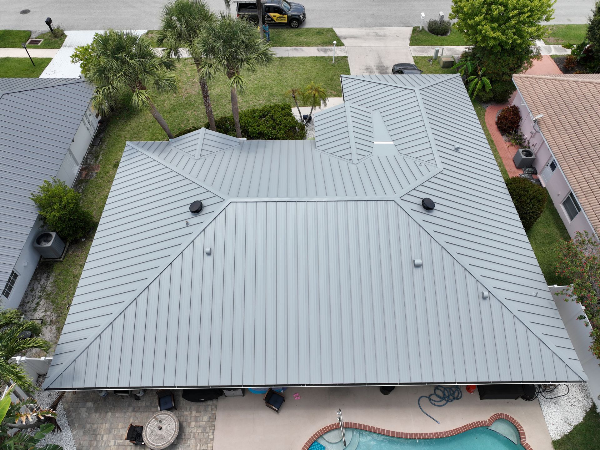 Aerial view of a gray metal roofed house, with a pool and some trees in the yard.