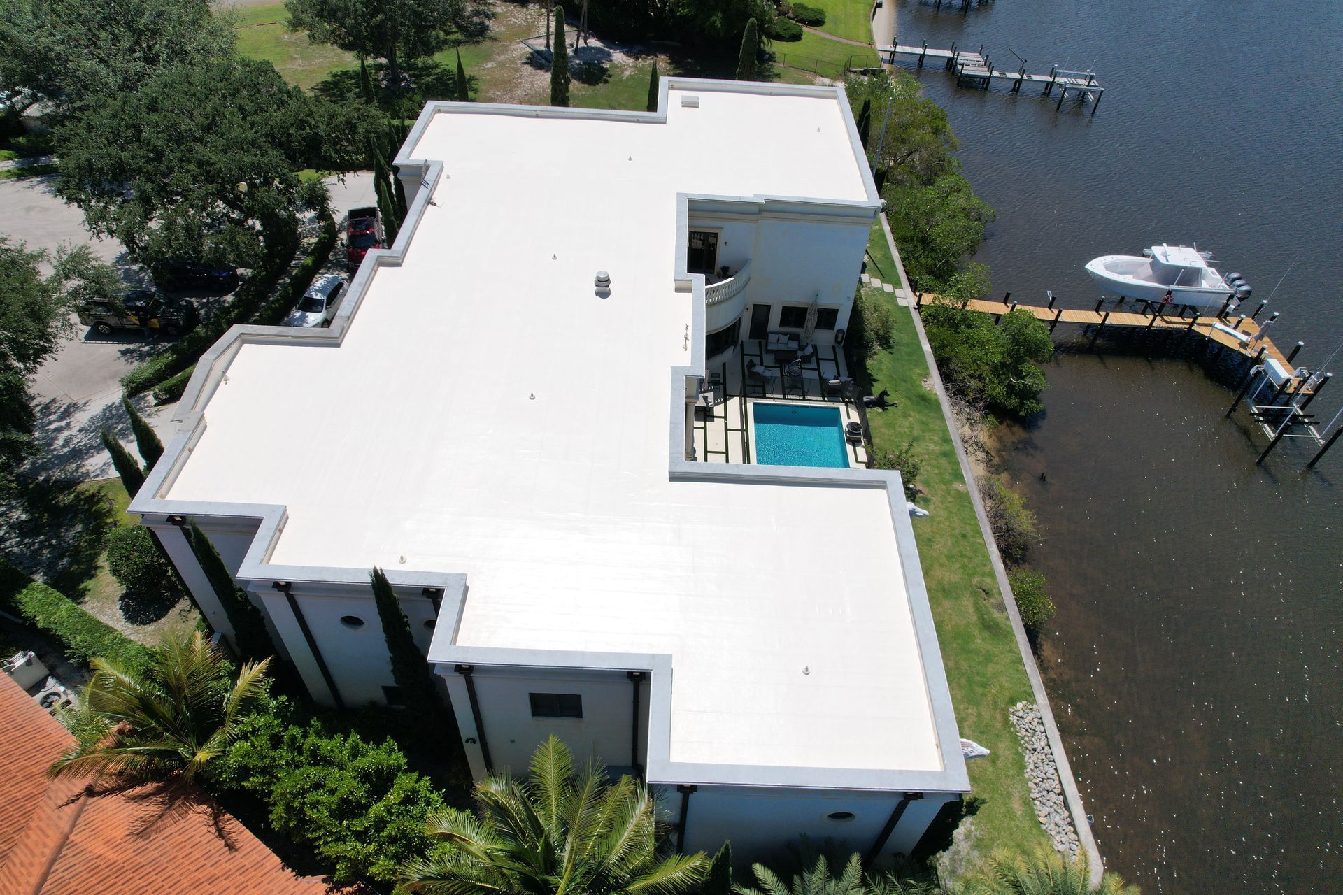 White house with flat roof, next to a body of water and dock; small pool visible.