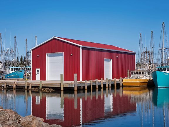 Red metal building and boat house sits at harbor edge.