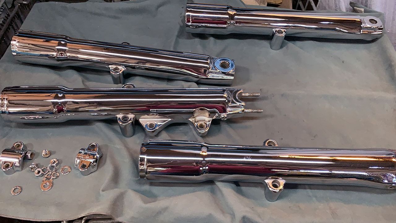 Tubos de escape cromados de motocicleta y pequeñas piezas de ferretería dispuestas sobre una superficie de tela.