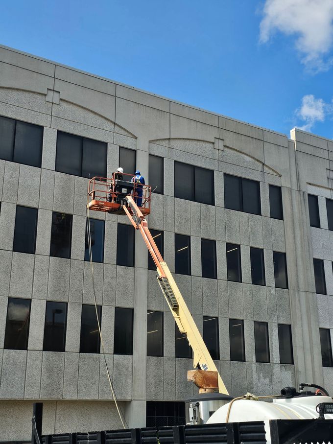 A blue work truck washing a driveway in front of a two-story house; a worker sprays the concrete.