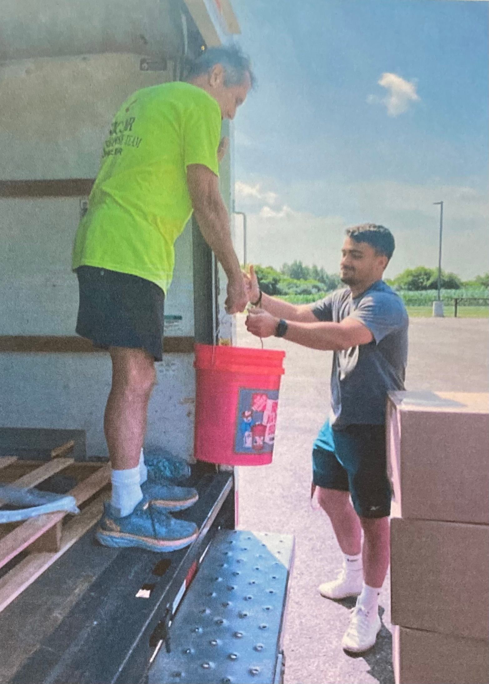 Two men are loading a red bucket into a truck.