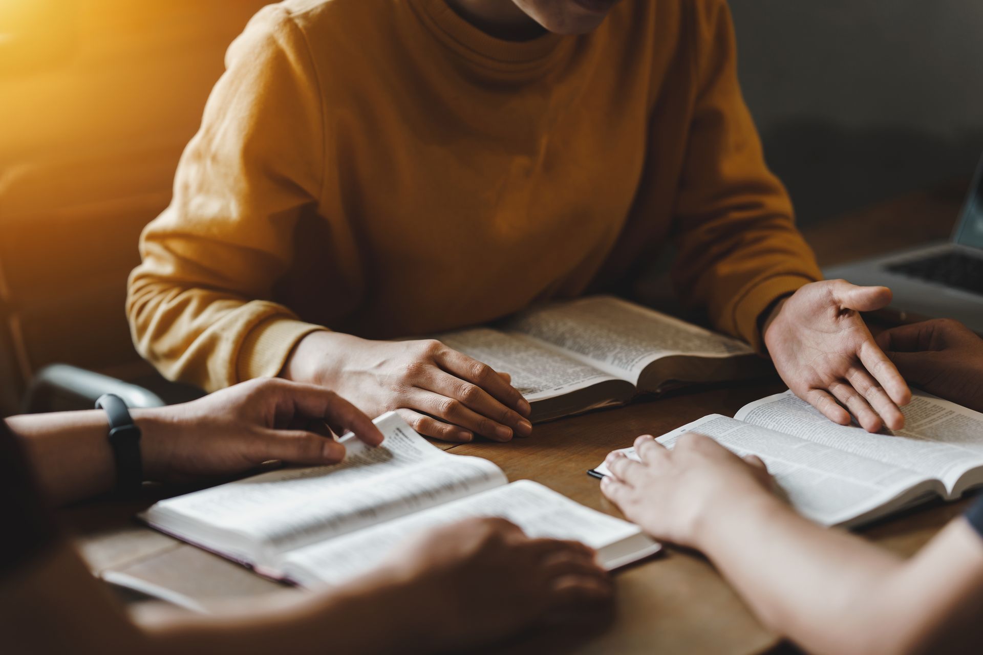 A group of people are sitting around a table reading bible.