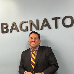 A man in a suit and tie is standing in front of a sign that says bagnato