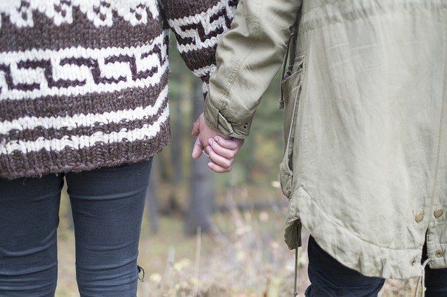 Two people are holding hands while walking in the woods.
