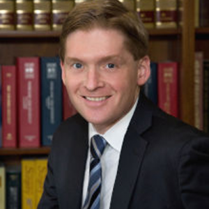 A man in a suit and tie is smiling in front of a bookshelf