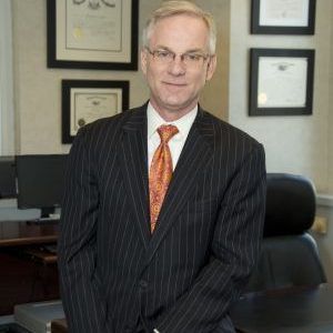 A man in a suit and tie is standing in front of a desk.