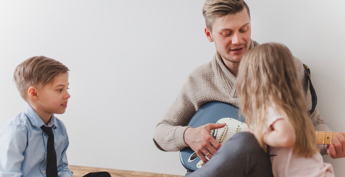 A man is playing a guitar to two children.