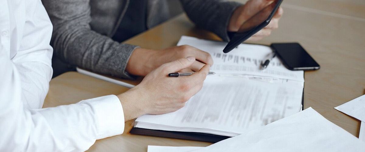 Two people are sitting at a table with papers and a cell phone.