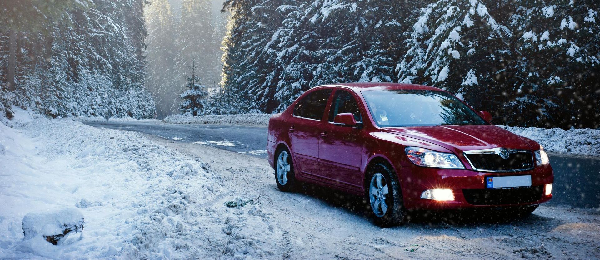 A red car is driving down a snowy road