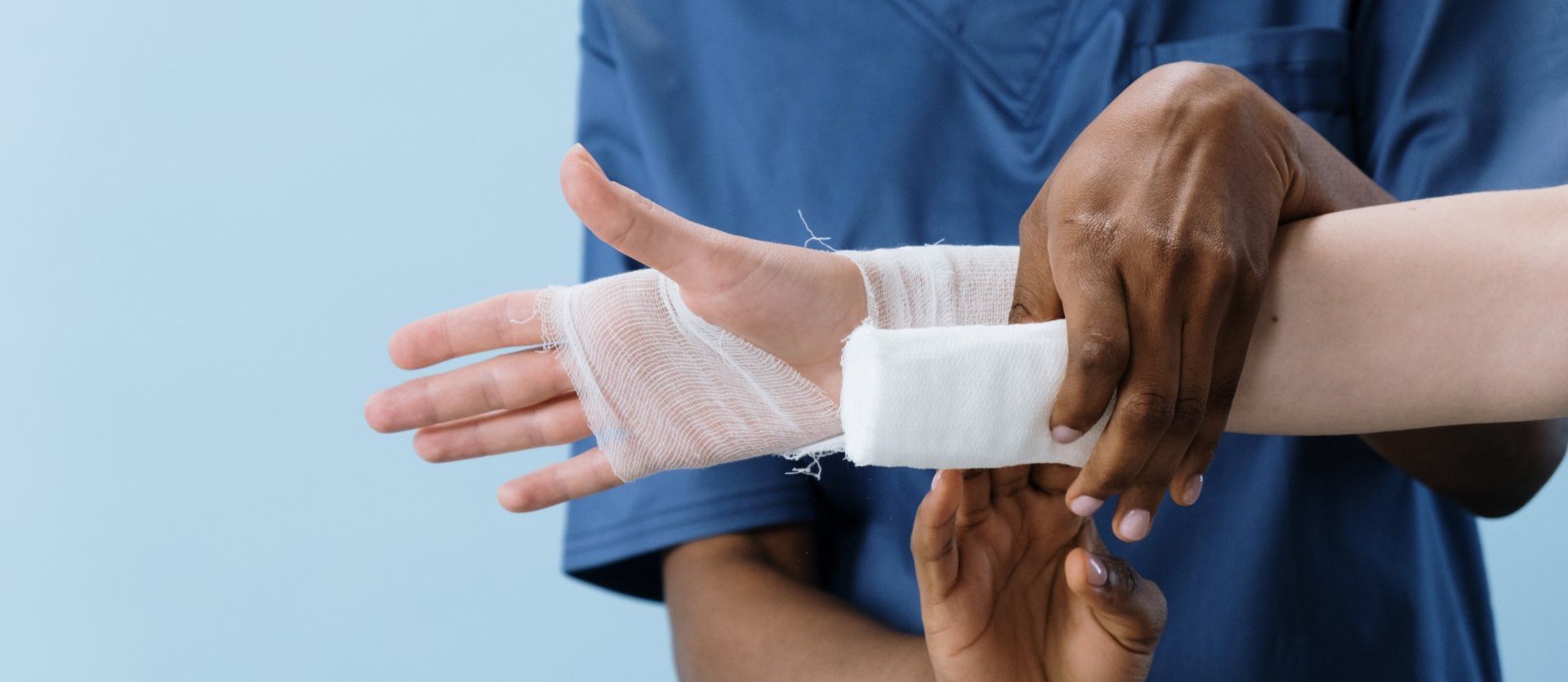 A nurse is wrapping a patient 's wrist with a bandage.