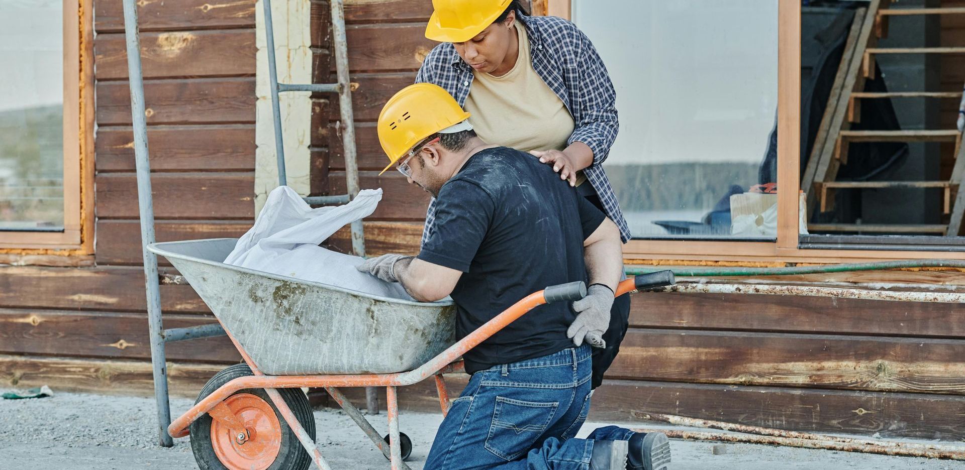 A man is pushing a wheelbarrow with a woman standing behind him.