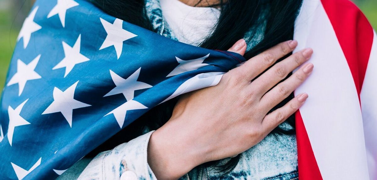 A woman holding an american flag with her hand on her chest