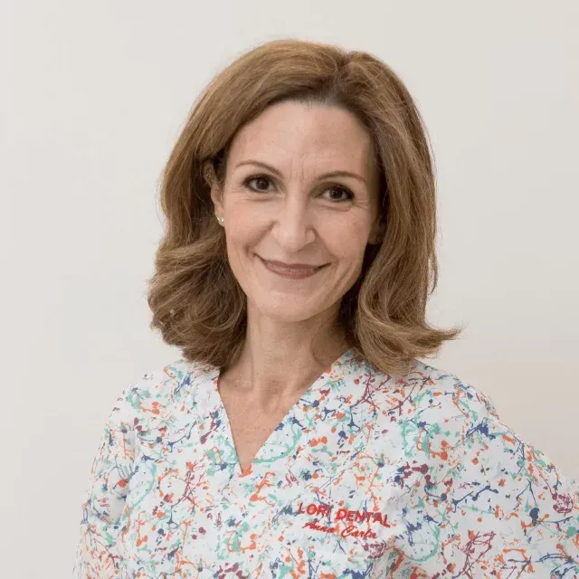 Un'odontoiatra sorridente con capelli castani di media lunghezza, che indossa una camice medico colorata e decorata.