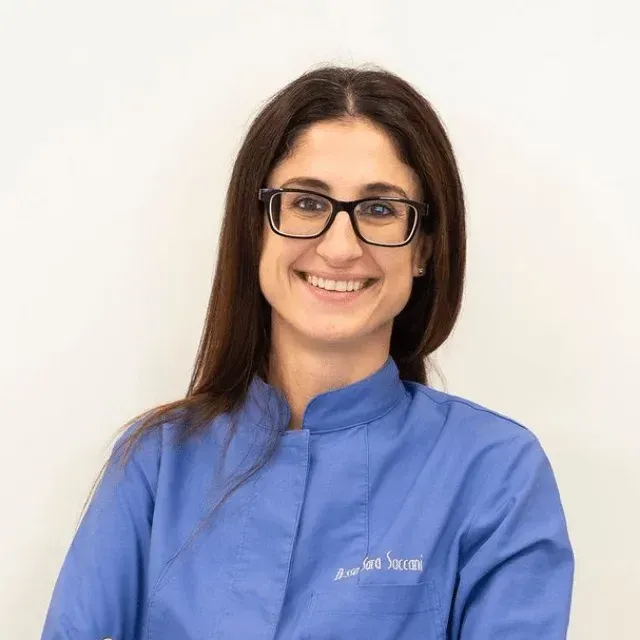 Un professionista sorridente con occhiali dalla montatura scura e una giacca blu da uniforme, su uno sfondo bianco uniforme.