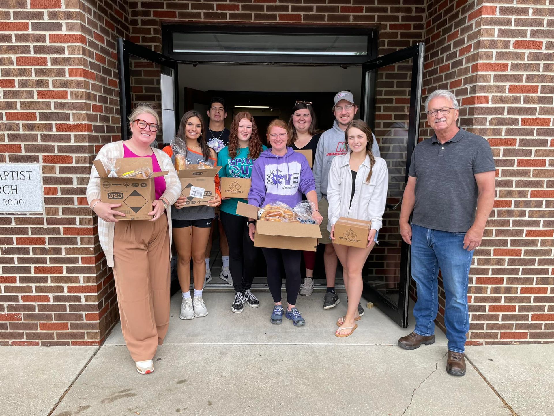 A group of people are standing in front of a brick building holding boxes.