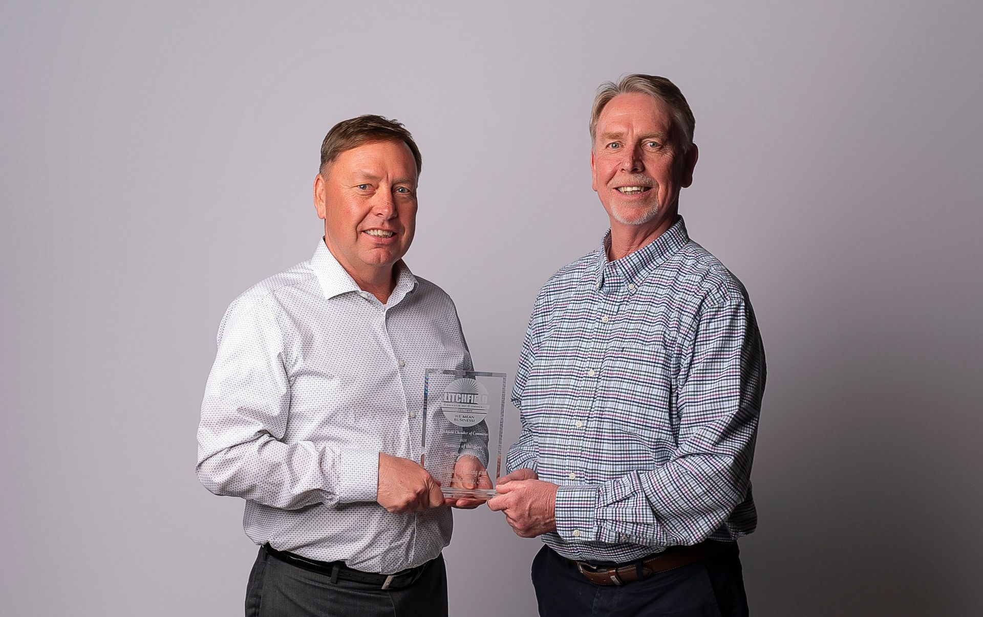 Two men are standing next to each other holding a trophy.