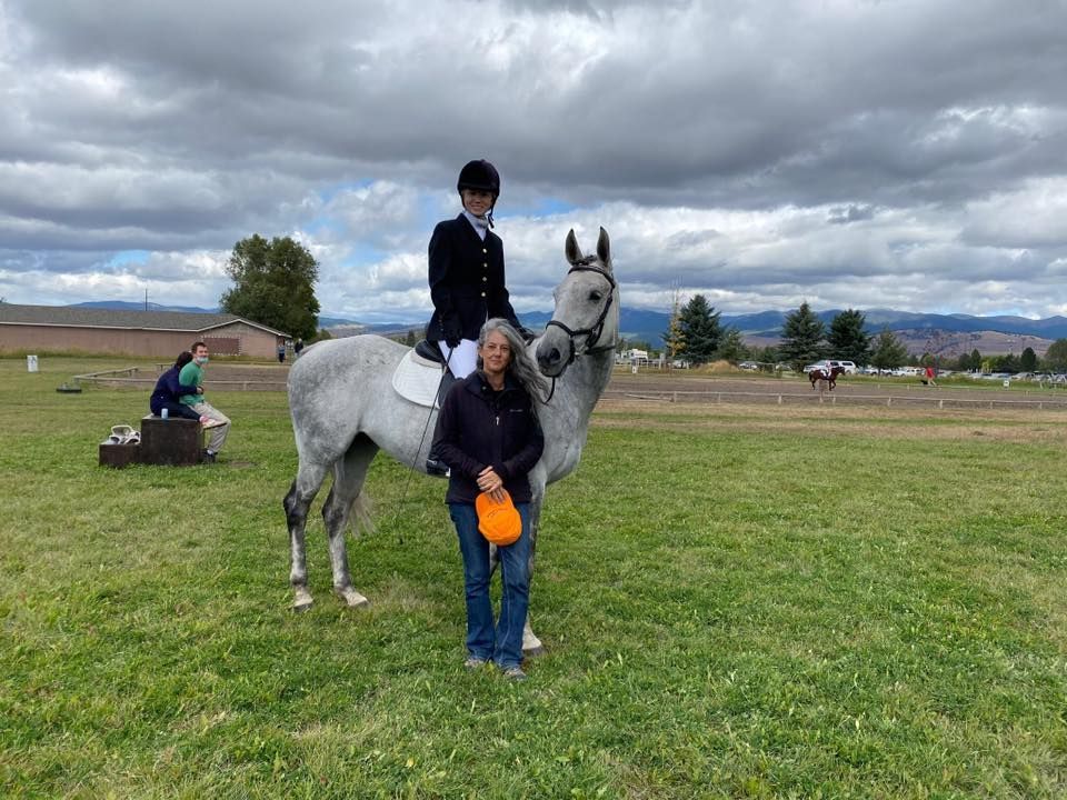 A woman is riding a horse in a field with a man standing next to her.