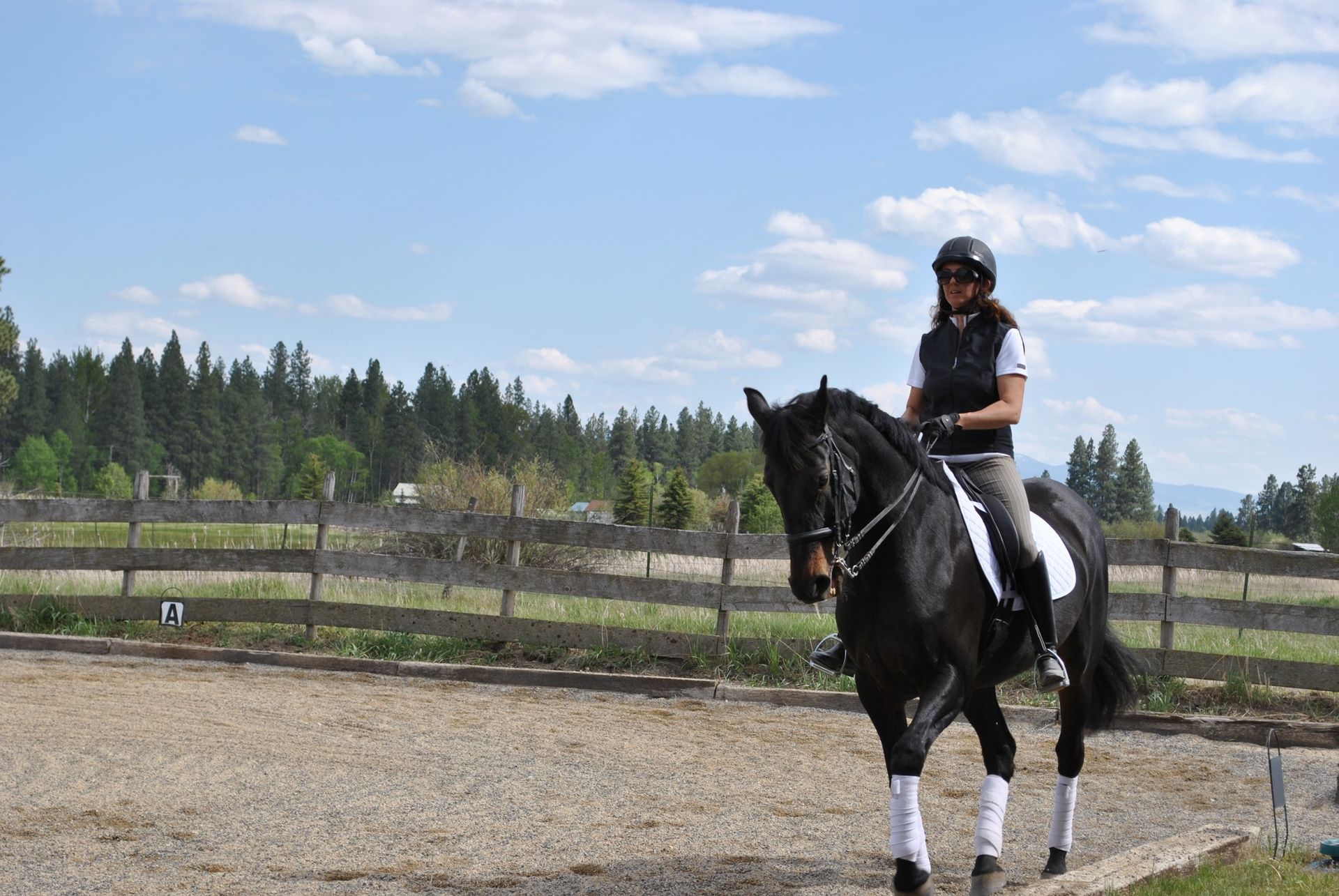A woman is riding a black horse in a dirt arena.