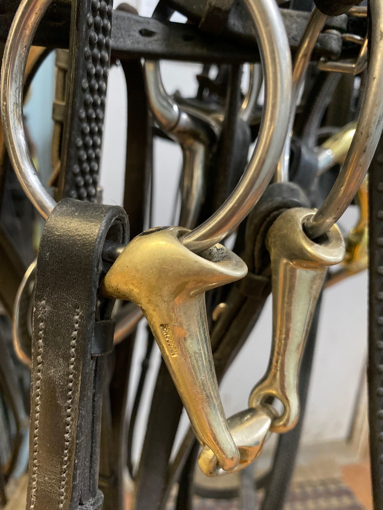 A bunch of horse bridles are hanging on a rack.