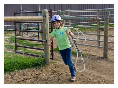 A young girl is holding a lasso in front of a fence.
