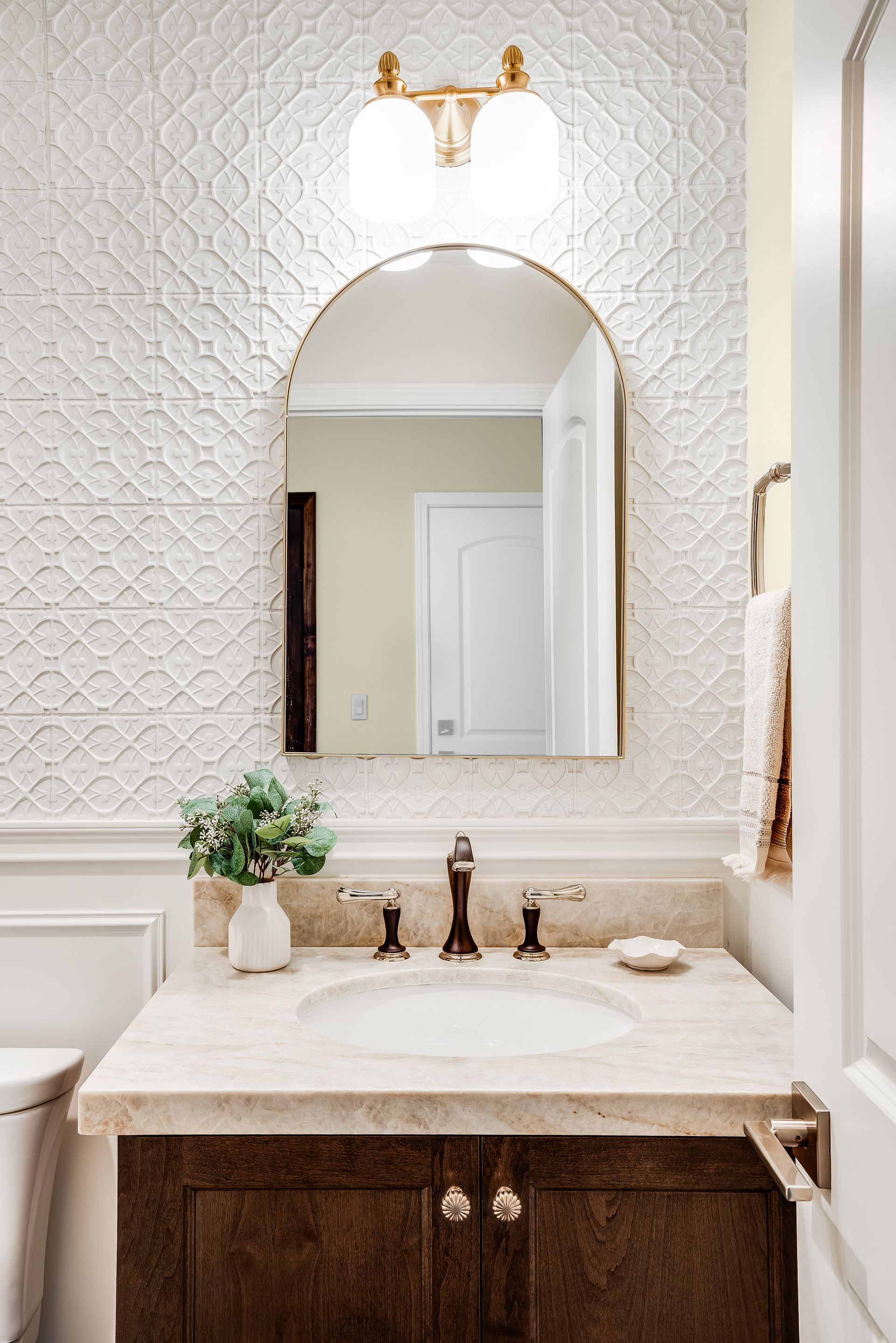 Bathroom with brown vanity, beige countertop, white sink, ornate mirror, and textured white wall.