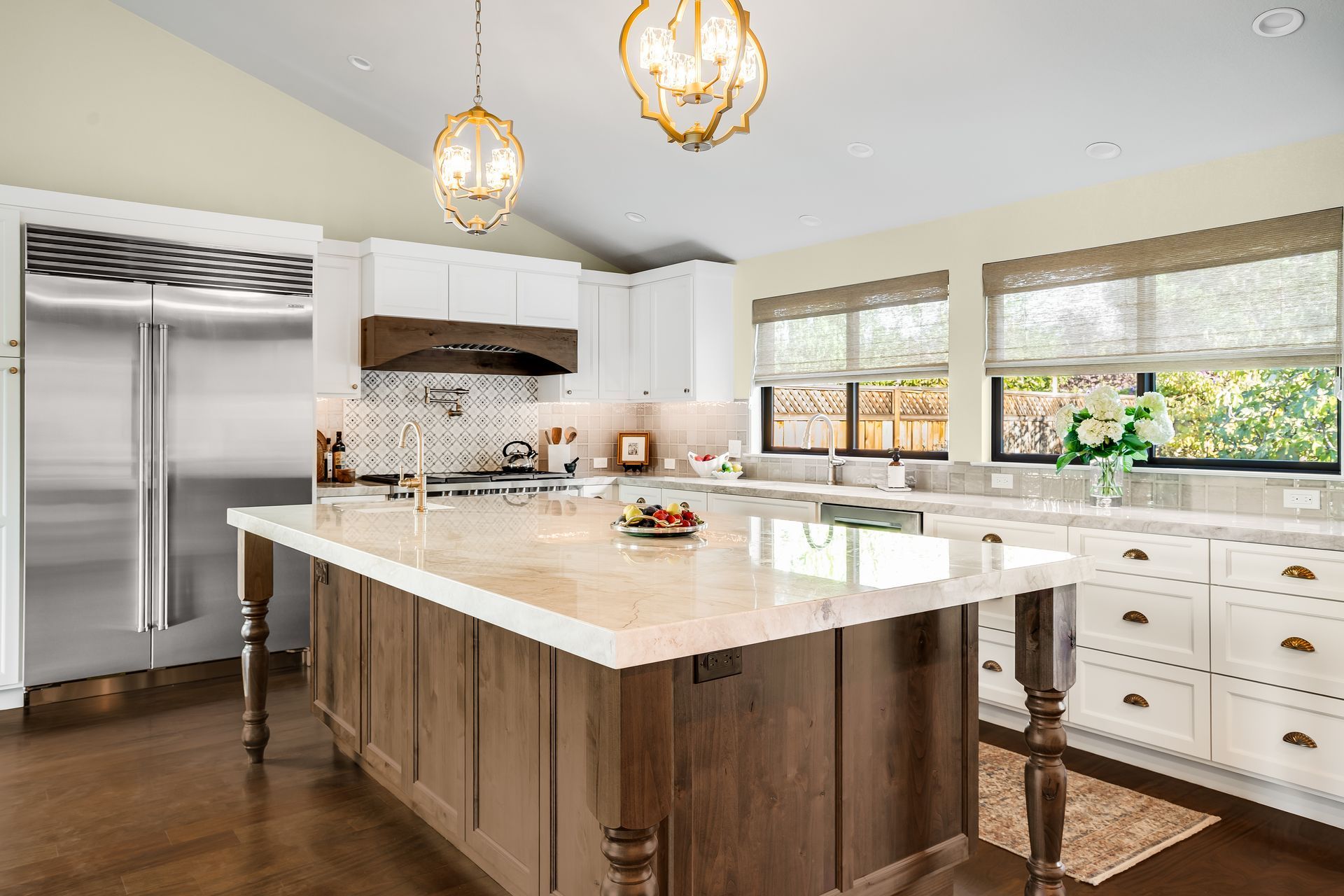 Bright kitchen with white cabinets, wooden island, stainless steel fridge, and large windows.