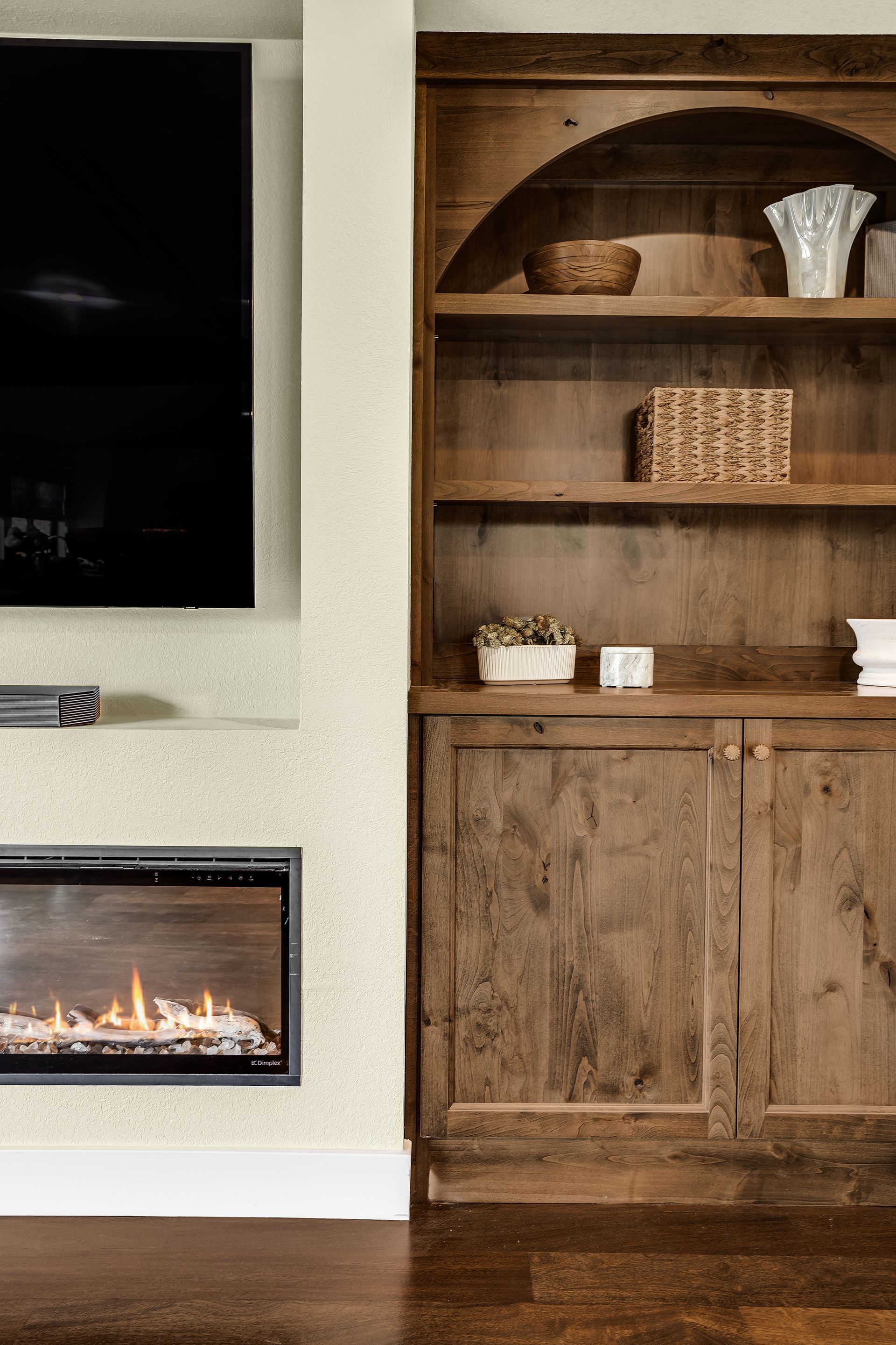 Fireplace with TV above and wooden bookcase. Warm brown tones and flame.