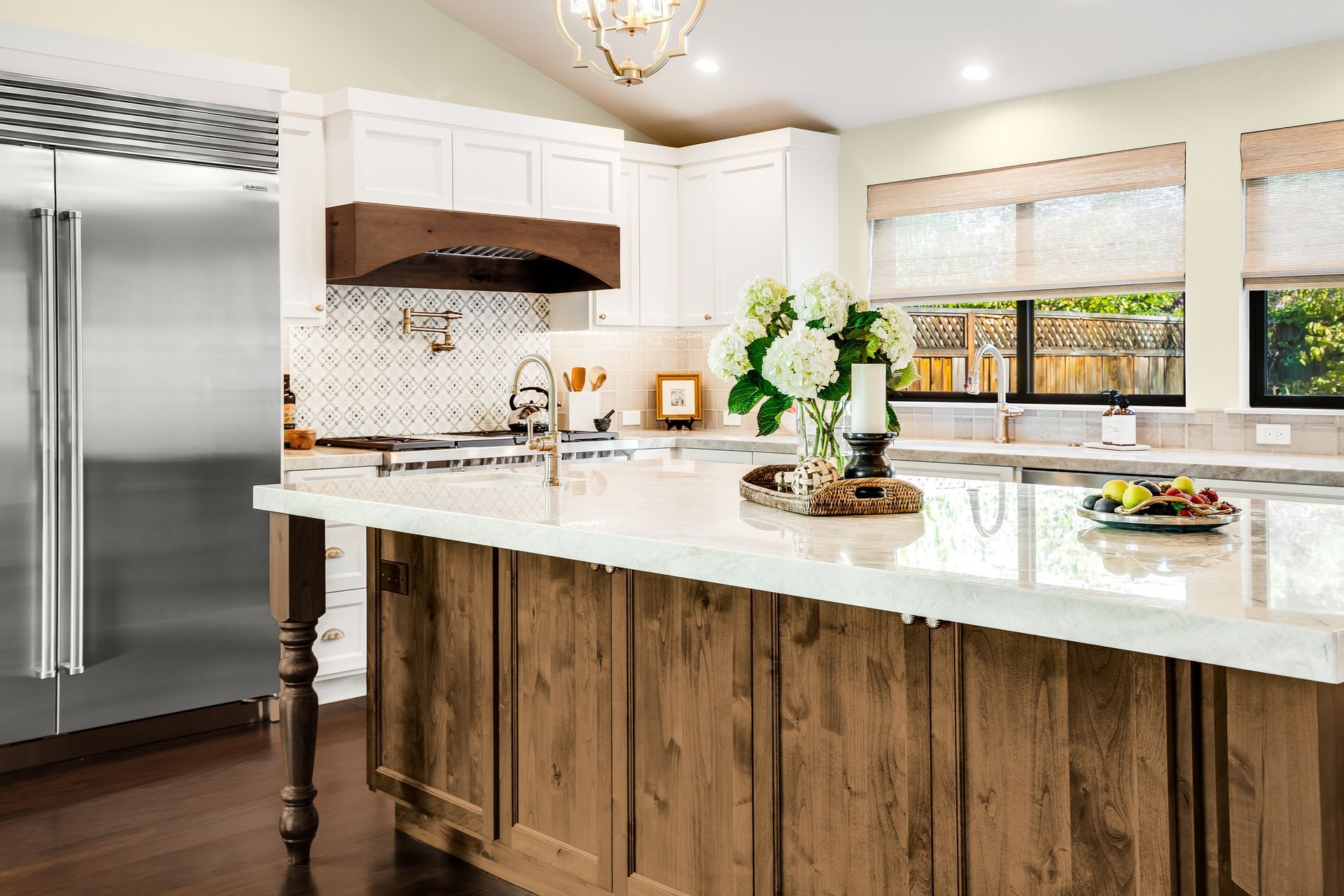 A bright kitchen with a wooden island, white countertops, stainless steel fridge, and flower bouquet.