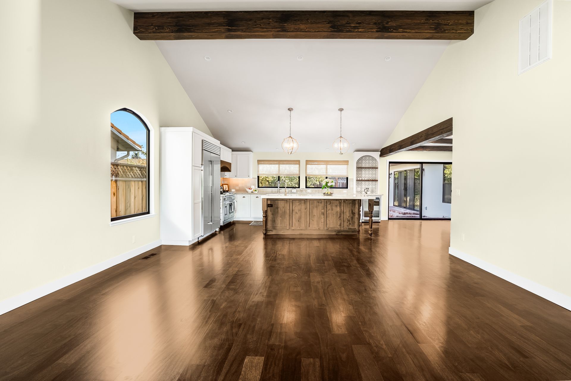 Spacious room with dark wood floor, a kitchen, and a bright vaulted ceiling with wooden beams.