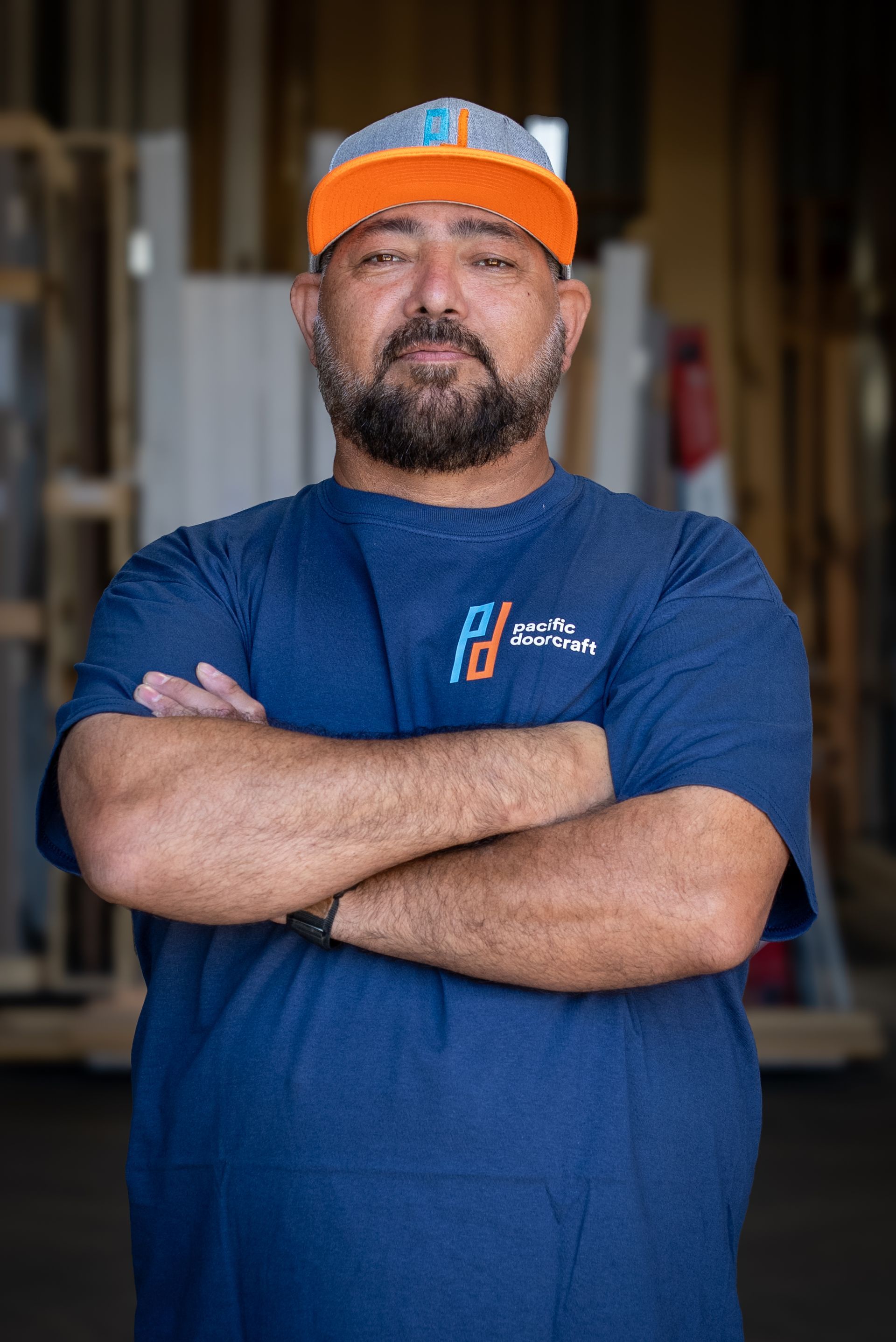 Man with crossed arms, wearing a cap and blue shirt, looking at the camera.