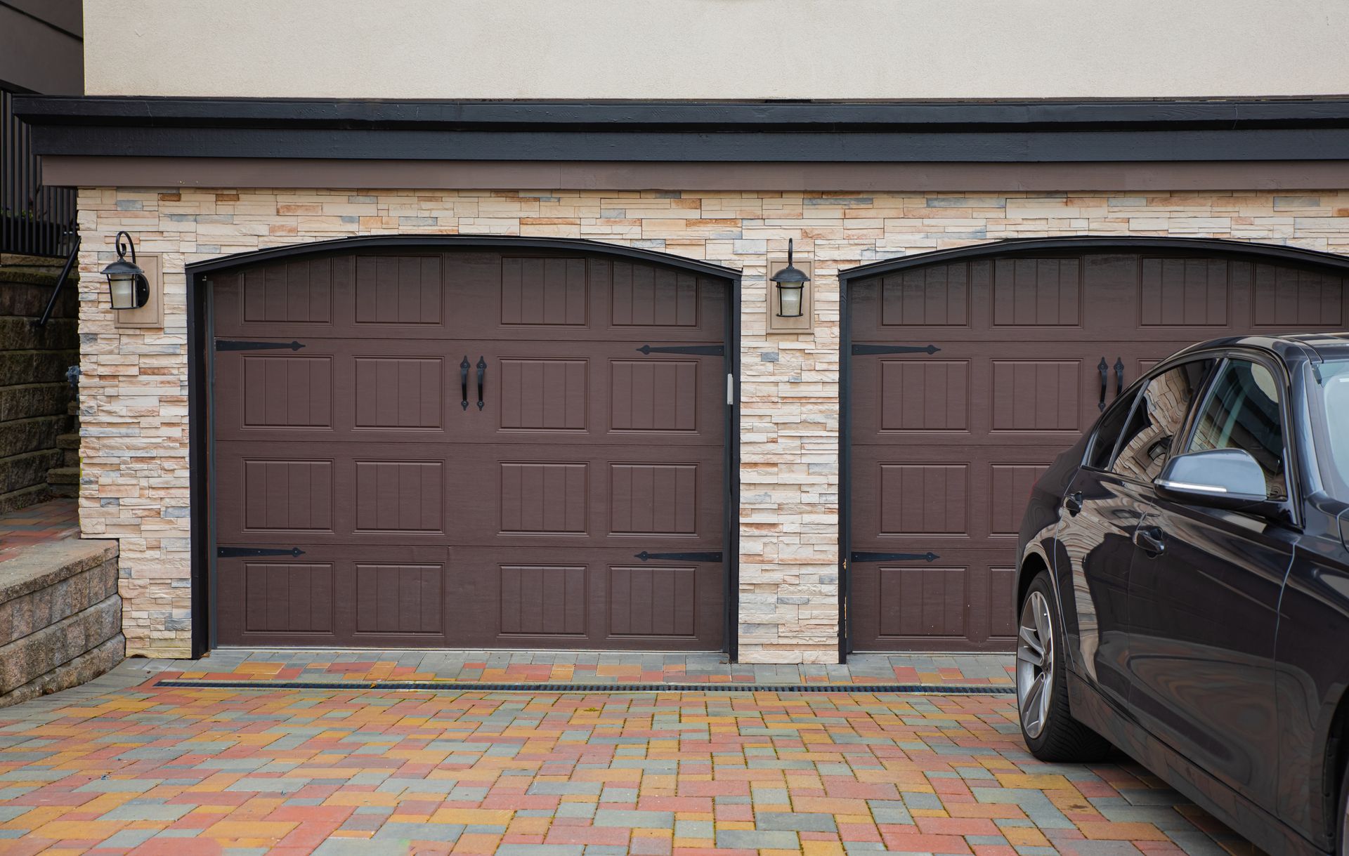 Brown garage doors with stone facade, car parked in driveway.